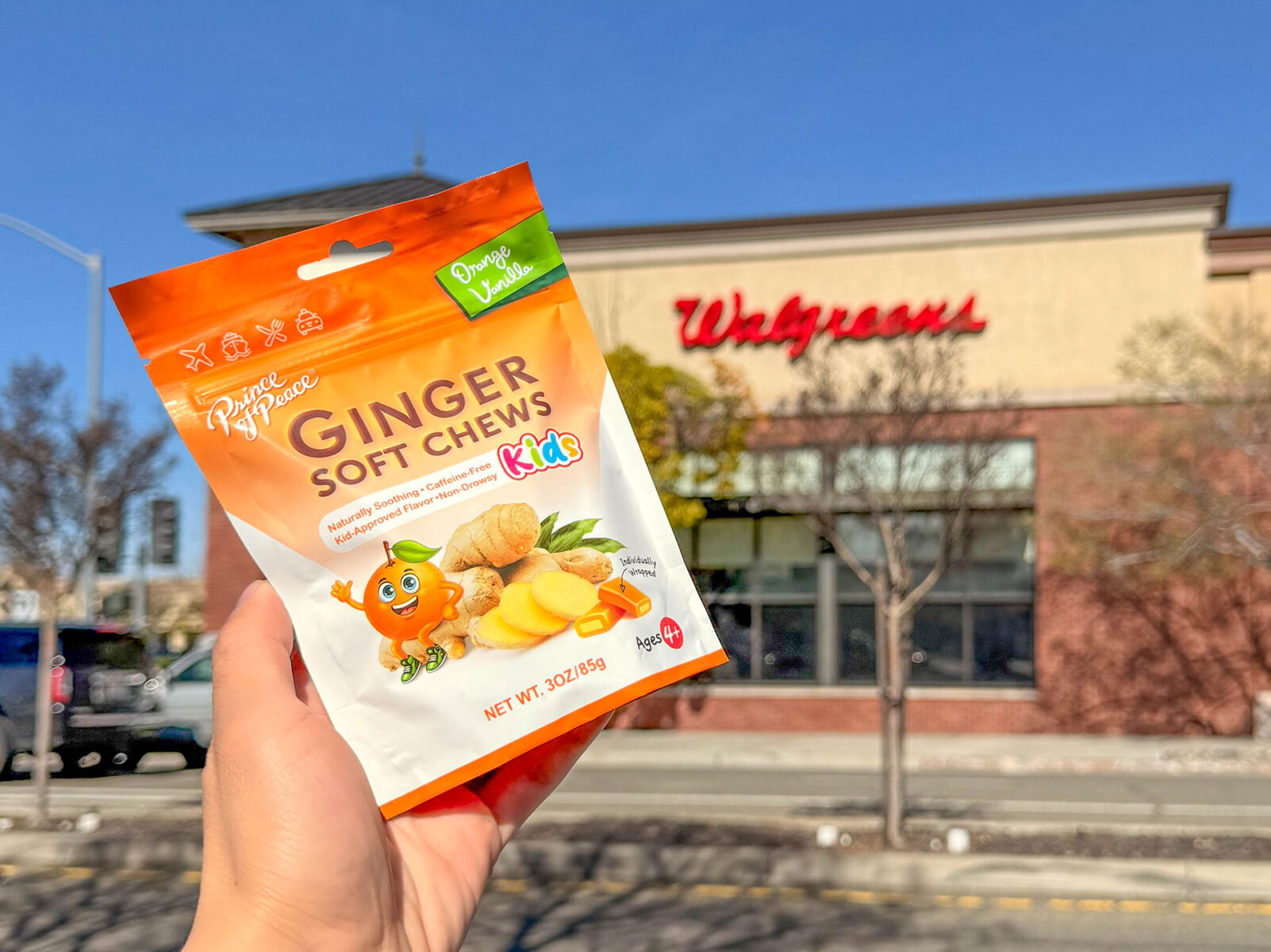 A Hand holding Prince of Peace Ginger Soft Chews for Kids in front of Walgreens storefront