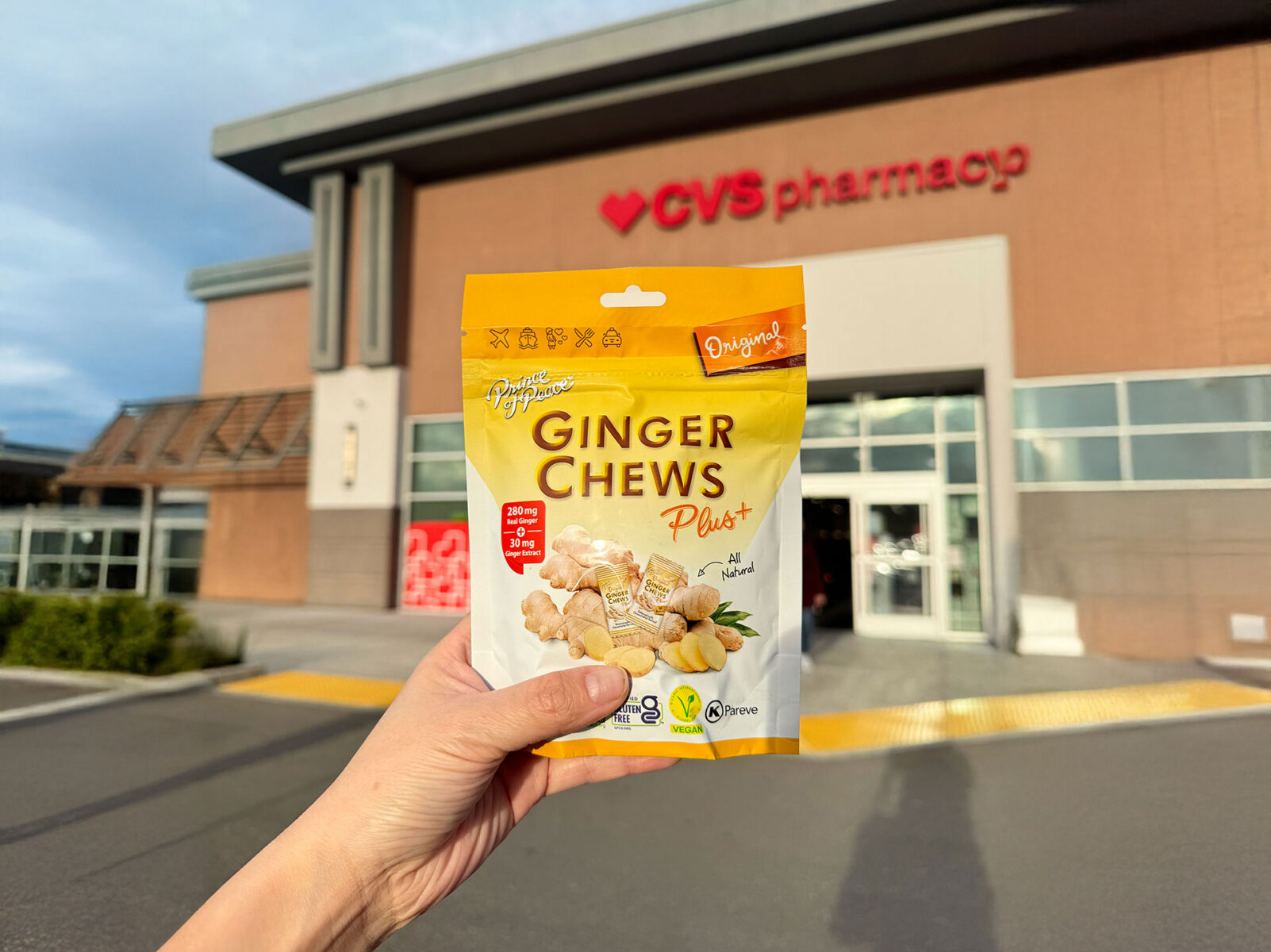 A hand holding pricen of peace ginger chews plus original flavor in front of a CVS pharmacy store